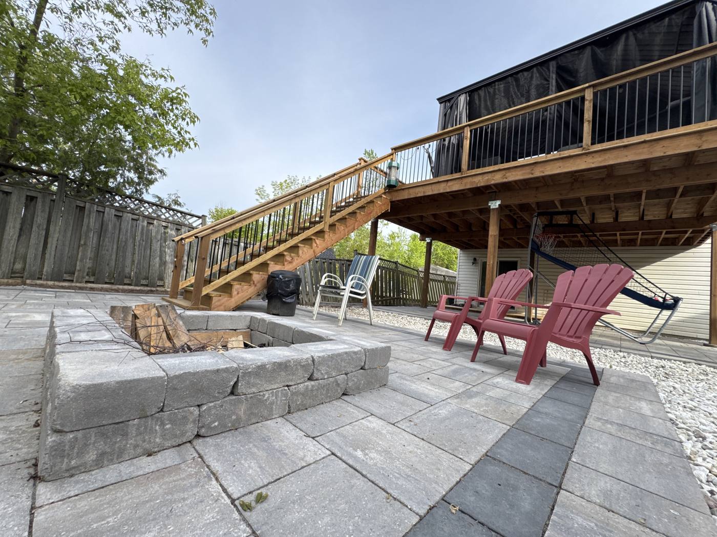 Stone fire pit with Adirondack chairs and a hammock on the patio under the deck