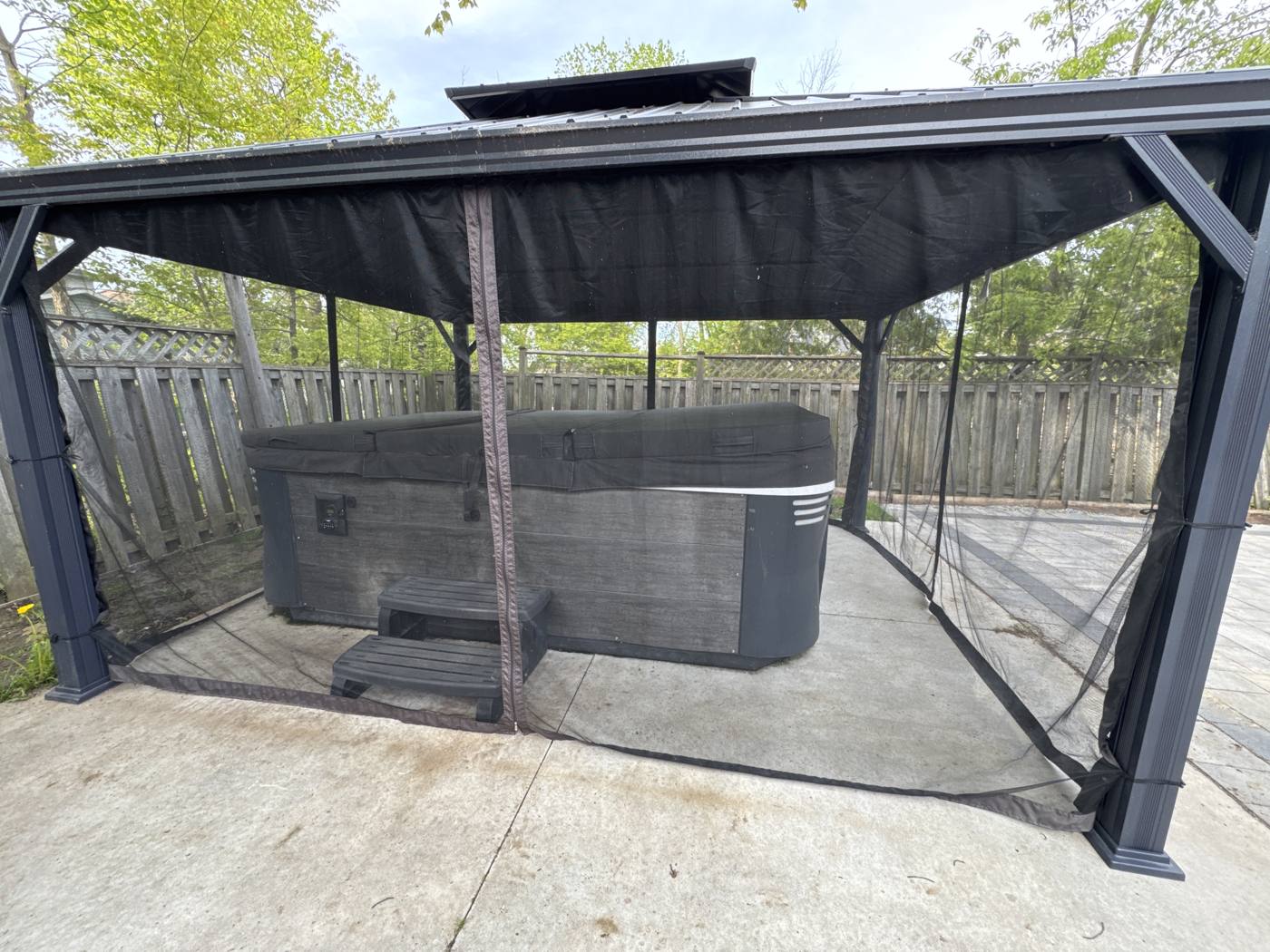 9-person hot tub under the black gazebo with privacy screens at the Innisfil cottage
